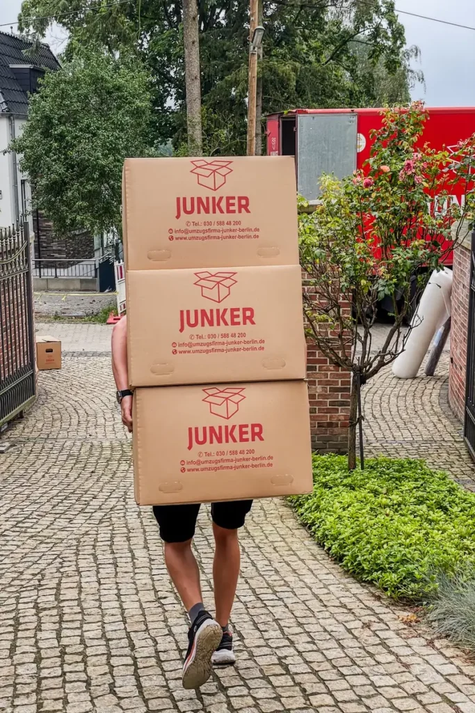 Umzugshelfer der Umzugsfirma Junker trägt drei gestapelte Umzugskartons beim Möbeltransport.