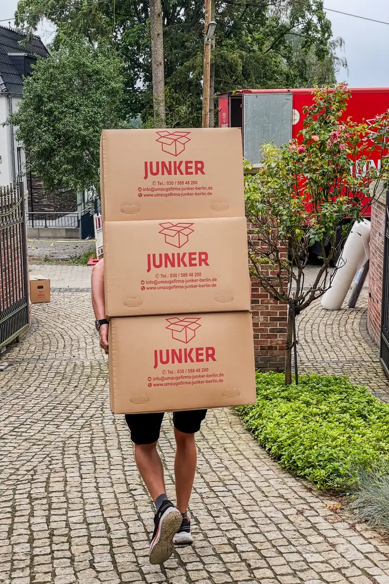 Junker-Mitarbeiter trägt gestapelte Umzugskartons im Freien