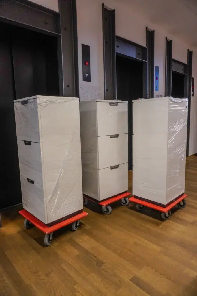 Mit Schutzfolie gesicherte Aktenschränke auf Rollbrettern vor dem Aufzug beim Firmenumzug