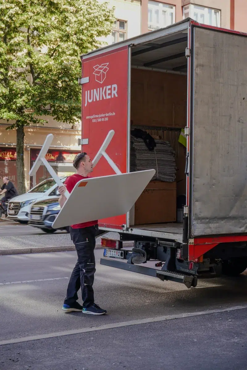 Mitarbeiter der Umzugsfirma Junker trägt einen umgedrehten Schreibtisch am LKW