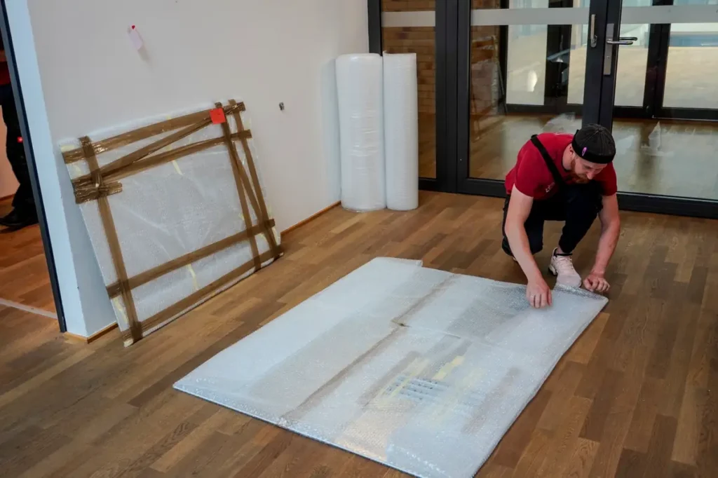 Mitarbeiter der Junker Umzugsfirma GmbH verpackt eine große Metallplatte mit Luftpolsterfolie