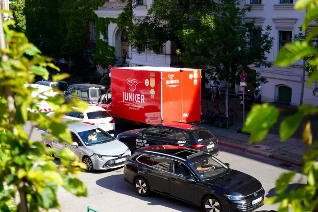 Der markante rote Umzugs-Lkw der Junker Umzugsfirma GmbH steht in einer Berliner Innenstadtstraße vor klassischer Altbaufassade. Das Bild zeigt die Professionalität und Präsenz des Unternehmens im Berliner Stadtgebiet.
