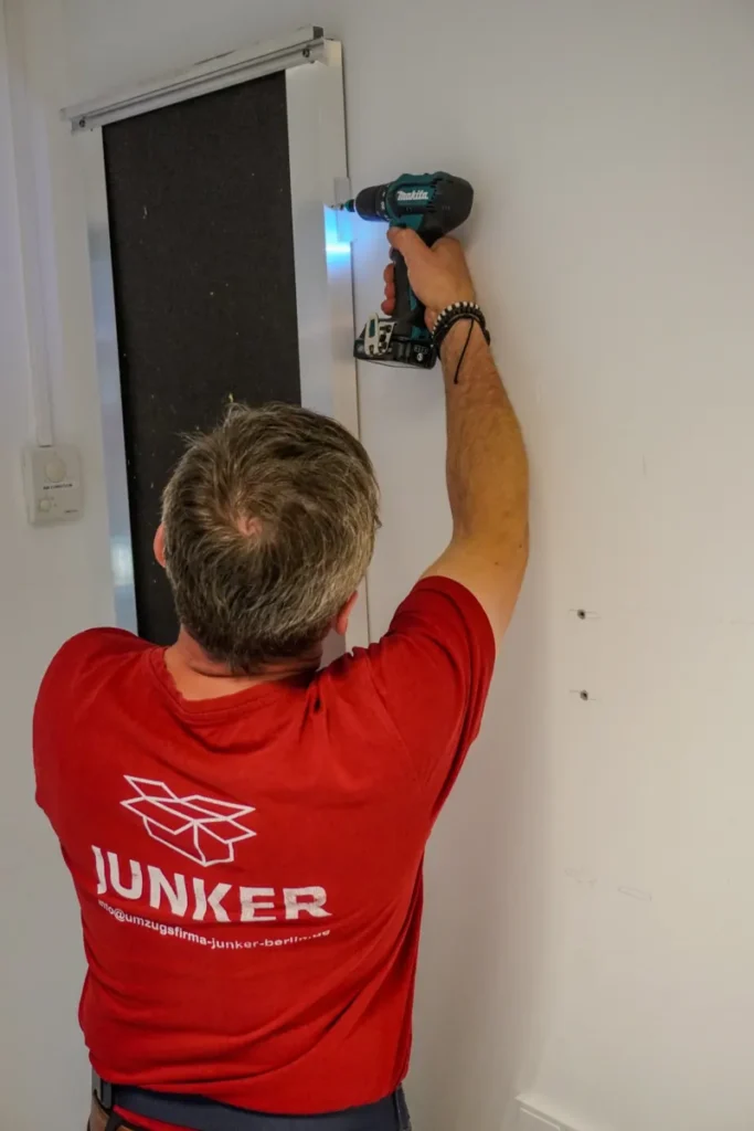 Mitarbeiter der Junker Umzugsfirma GmbH montiert ein Wandmodul mit einem Akkuschrauber