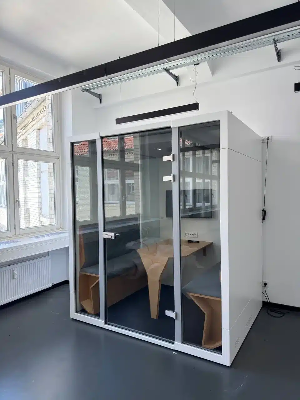 Glass-fronted office pod with a table and seating beside large windows